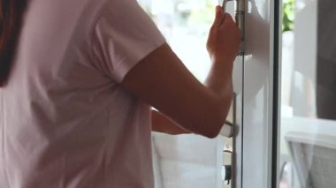 Açık pembe gömlekli bir kadın modern bir sürgülü cam kapı açar, açık hava terası ve beyaz mobilyaları gün ışığında ortaya çıkarır.