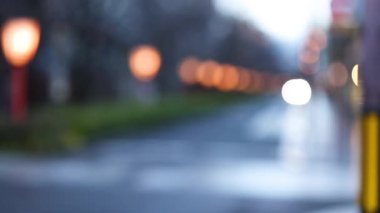 Islak bir şehir caddesi boyunca odak dışı ışıklar