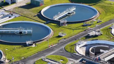 Hava görüntüleri modern bir atık su arıtma tesisinde günışığında dairesel yerleşim tanklarını, su kanallarını ve endüstriyel altyapıyı aydınlatıyor.
