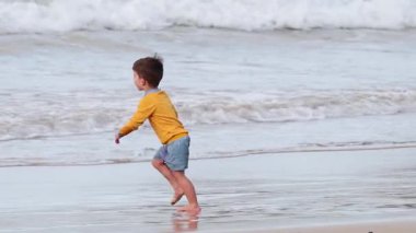 Bir çocuk kumsalın ve dalgaların tadını çıkarır.
