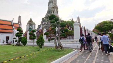 Turistler Wat Arun, Bangkok 'ta yürürken, yumuşak gün ışığında tapınağın mimarisini ve canlı atmosferini yakalıyorlar.