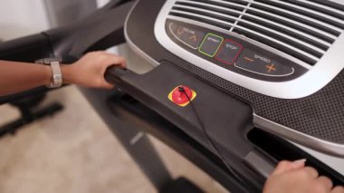 Bir kadın evdeki spor salonunda koşu bandı kontrol paneliyle etkileşime giriyor, içerideki sıcak ışık altında ayarları ayarlıyor.