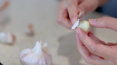 Mutfak tezgahında sarımsak karanfilleri soyan, yumuşak ışıklandırmalı ve nötr arka planlı eller.