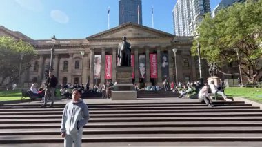 İnsanlar Melbourne Devlet Kütüphanesi 'nin önünde dinleniyor.