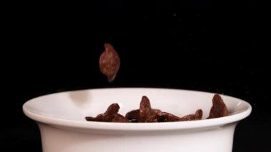 Çikolatalı gevrek parçaları siyah arkaplana karşı beyaz bir kaseye taşarak dinamik ve iştah açıcı bir görsel yaratıyor.