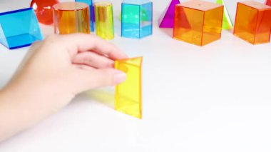 Bir el, beyaz bir yüzey üzerinde canlı üç boyutlu geometrik şekilleri manipüle ederek hareket ve etkileşimi parlak bir ortamda gösterir.