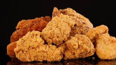 Çeşit çeşit kızarmış tavuk kanatları, but ve nuggetların yansıtıcı siyah bir yüzey üzerinde, sıcak stüdyo ışıklarıyla aydınlatılmış dönüşümlü bir görüntüsü.