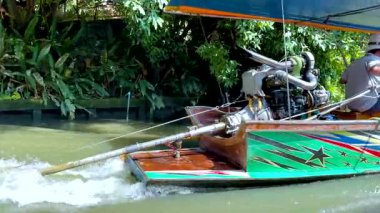 Canlı bir motor teknesi Bangkok 'un yemyeşil bir kanalında hızla ilerler, parlak gün ışığında yerel hayatı ve dinamik hareketleri gözler önüne serer.