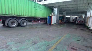 Yeşil konteynırlı büyük bir kamyon Koh Samui, Tayland 'da bulutlu gökyüzünün altında bir feribota biniyor.