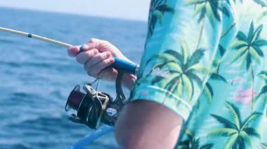 Tropikal tişörtlü bir adam Tayland 'ın güneşli Phuket şehrinde sakin okyanus çevresindeki bir tekneden balık tutar.