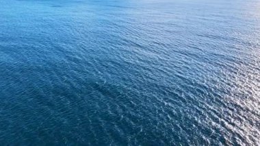 Sakin, derin, mavi okyanus suyunun statik geniş bir görüntüsü. Güneş ışığı hafif dalgalardan yansıyor. Doğal ışıklandırma, görünür bir arazi ya da nesne yok, sakin bir ruh hali.