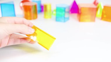 Eller, parlak ve eğitici bir ortamda geometri ve renkleri vurgulayarak, beyaz bir yüzeyde canlı üç boyutlu şekilleri manipüle eder.