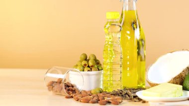 Yağlar, fındıklar ve avokadolar dahil olmak üzere çeşitli sağlıklı yağlar, sıcak ışıklandırmalı ahşap bir masaya dizilmiştir.