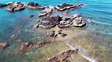 İnsansız hava aracı kamerası güneşli sahil kaya oluşumları ve berrak turkuaz suyun üzerinde süzülerek gelgit havuzlarını ve Avustralya, Port Douglas yakınlarındaki engebeli dokuları ortaya çıkarıyor.