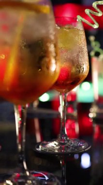 Dolgun bir tezgahın üzerinde narenciye ile süslenmiş buzlu kokteyller. Canlı, renkli gece hayatı aydınlatması ve sığ bir alan derinliği ile aydınlatılmış.