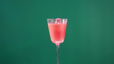 Pembe bir kokteyl çiçeklerle süslenir yeşil ekran arkaplanı karşısında maşa kullanılır, canlı renkler ve hassas hareketler vurgulanır.