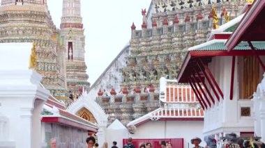 Turistler Bangkok 'taki Wat Arun Tapınağı' nın etrafında dolaşıp, karmaşık mimarisini yakalıyorlar. Parlak gün ışığı tapınağın detaylı tasarımını güçlendirir.