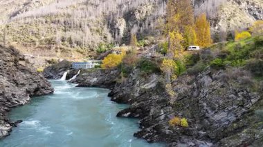 İnsansız hava aracı görüntüleri Kawarau Nehri 'nin turkuaz sularını ve Queenstown, Yeni Zelanda' daki bir hidroelektrik santralinin yakınındaki sonbahar yeşilliklerini yakalar.