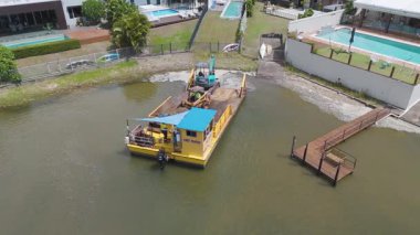 Broadbeach Waters, Queensland 'daki lüks evlerin yakınındaki bir kanalda çalışan makineli bir mavnanın hava görüntüsü.