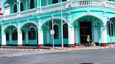 Motosikletler Tayland, Phuket 'te canlı bir turkuaz koloni binasının önünden geçiyor. Parlak gün ışığı sahnenin canlı atmosferini arttırır.