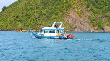 Bir balıkçı teknesi Tayland 'ın Phuket kentindeki yemyeşil bir adanın yakınındaki sakin sularda yüzer. Parlak gün ışığı dingin okyanus manzarasını güçlendirir.