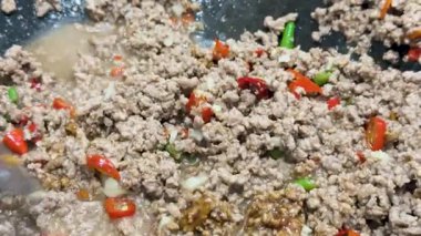 Domuz eti, kırmızı biber ve otlar, parlak ışık altında sıcak bir tavada kızartılır. Dinamik spatula hareketi ve yakın çekim kamera açıları vardır.