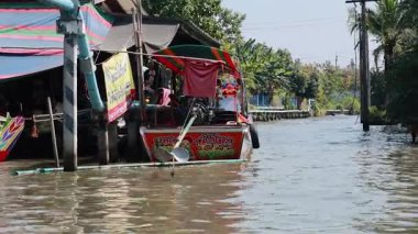 Canlı tekneler Bangkok, Tayland 'da hareketli bir kanal pazarından geçiyor. Parlak renkler ve güneşli gökyüzünün altında canlı bir atmosfer