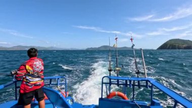 Bir balıkçı teknesinde Ko Racha Yai yakınlarındaki sularda, berrak gökyüzü ve parlak güneş ışığı altında gezinen bir insan.