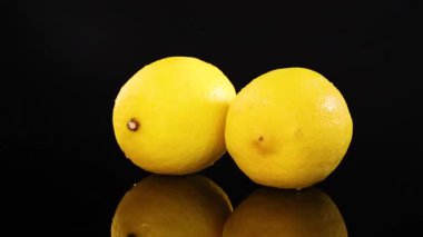 İki limon parlak ışık altında parlak siyah bir yüzey üzerinde dönerek canlı ve dinamik bir görsel etki yaratır.