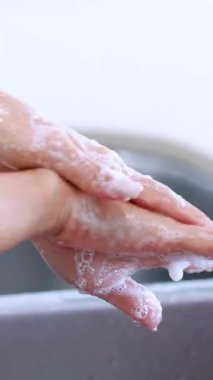 Parlak bir mutfakta sabunla yıkanan ve akan suyun altında durulanan eller, hijyen ve uygun temizlik tekniklerini vurgular.