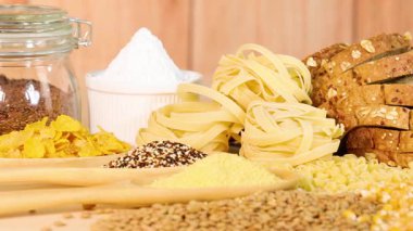 Tahta bir masaya yerleştirilmiş tahıl, makarna ve dilimlenmiş ekmek çeşitleri.