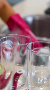 Pembe eldiven giyen biri, mutfak lavabosunda sabunlu suyla bardakları yıkıyor.