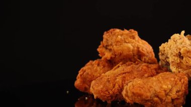 Çeşitli kızarmış tavuk kanatları, but ve nuggetlar sıcak, stüdyo ışıkları altında yansıtıcı siyah bir yüzey üzerinde döner, çıtır çıtır dokular ve altın rengi vurgular.