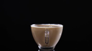 Kahveyle dolu bir cam bardak, zarif tasarımını ve zengin rengini vurgulayarak, koyu bir arkaplana doğru düzgün döner.