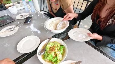 İki kişi Champasak, Laos 'ta bir restoranda pirinç ve sebzeyle yemek yiyor. Parlak, doğal ışık canlı atmosferi güçlendirir.