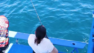 Tayland, Phuket 'te bir tekneden balık avlıyor, sakin okyanus manzarası ve odaklanmış balıkçılık hareketleri sergiliyor.