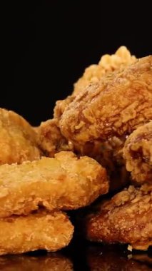 Altın kızarmış tavuk kanatları, but ve nuggetlar stüdyo ışıkları altında parlak siyah bir yüzey üzerinde döner, çıtır çıtır dokular ve iştah açıcı detaylar vurgular