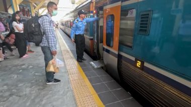 Banliyö ve turistler gün ışığında kapalı bir platformda mavi bir trene biniyorlar, istasyon personeli de yardımcı oluyor ve doğal olarak ışık yayılıyor.