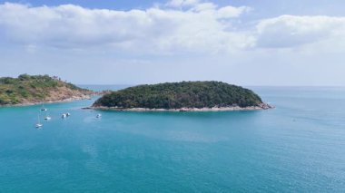 İnsansız hava aracı Phuket, Tayland 'daki huzurlu ada koyunu görüntülüyor. Açık gökyüzü ve turkuaz sular sakin bir manzara yaratır.