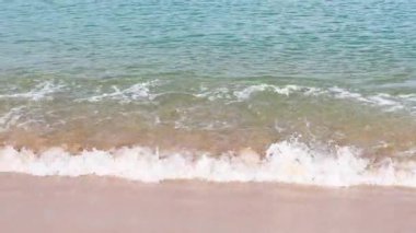 Dalgalar, parlak gün ışığında kumlu bir sahile yavaşça yuvarlanarak sakin bir sahili yakalar.