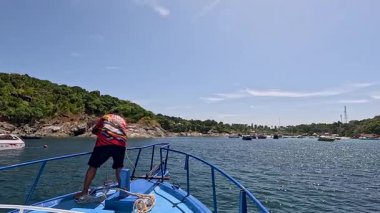 Bir adam, Phuket, Tayland 'daki geleneksel bir teknede, güpegündüz bereketli sahil manzaralı bir demir atar.