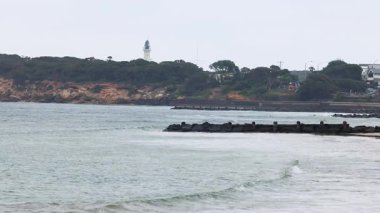 Sakin okyanus dalgaları Lonsdale Burnu deniz fenerine doğru ilerliyor bulutlu gökyüzünün altında, sakin bir sahil manzarası yaratıyor.