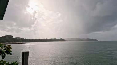 Geniş açılı bir çekim, denizi aşıp Ko Phayam 'daki orman kıyı şeridine doğru hareket eden, kayan bulutlar ve değişen ışıkla dramatik bir yağmur fırtınası yakalar.