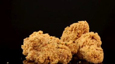 Altın renginde kızarmış tavuk göğsü ve kalçaları ağır çekimde siyah arka plana doğru döner ve kıtır kıtır kıtır ve baharatlı baharat içerir.