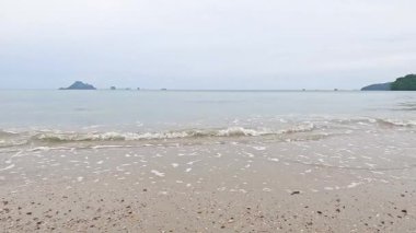 Nopparat Thara Sahili 'nde yumuşak ve bulutlu bir ışık altında dalgaların kıyıya vuruşunun sakin bir görüntüsü.