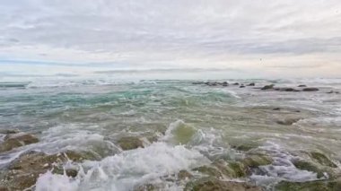 Dalgalar ağır çekimde kayaların üzerine düşüyor.