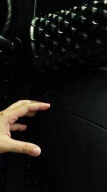 Eller spor salonunun rafından mavi pilates topuna uzanır ve onu çıkarır. Bu da direnç bantlarını ve köpük rulolarını ortaya çıkarır. Parlak, odaklanmış ışık altında sabit kamera hareketleriyle.