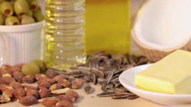 Ayçekirdeği, parlak stüdyo ışıklarında badem, zeytin, tereyağı, hindistan cevizi ve yağlı bir masaya düşer. Statik kamera, canlı yemek düzenlemesi.