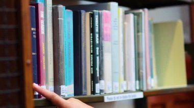 Kütüphane rafından elle bir kitap seçiyor