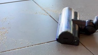 Elektrikli süpürge, doğal güneş ışığı altında fayanslı zeminden enkazı temizler. Etkili temizlik hareketleri sergiler.
